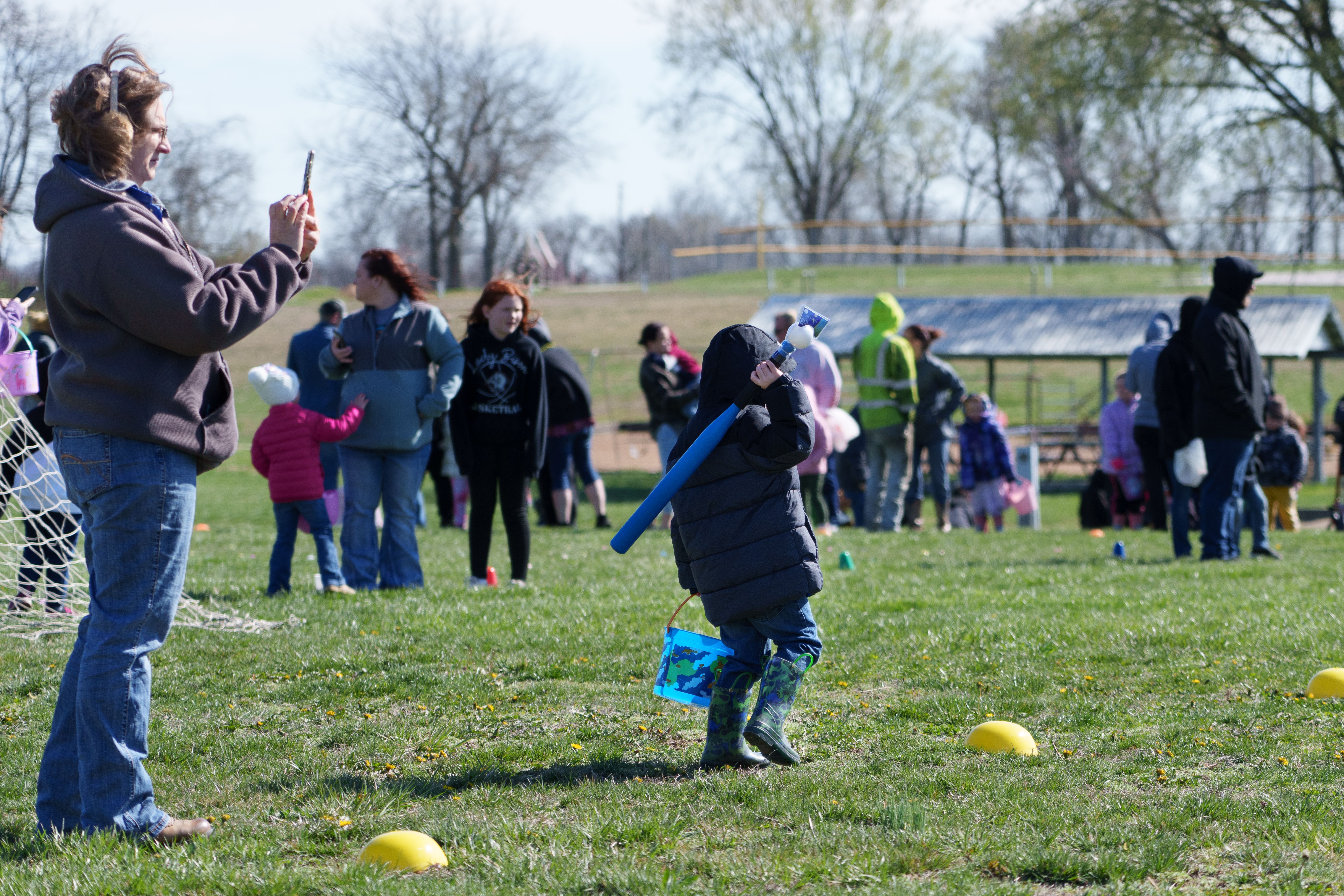 Photo of a child carrying a baseball bat and bucket, waiting at the edge of the field