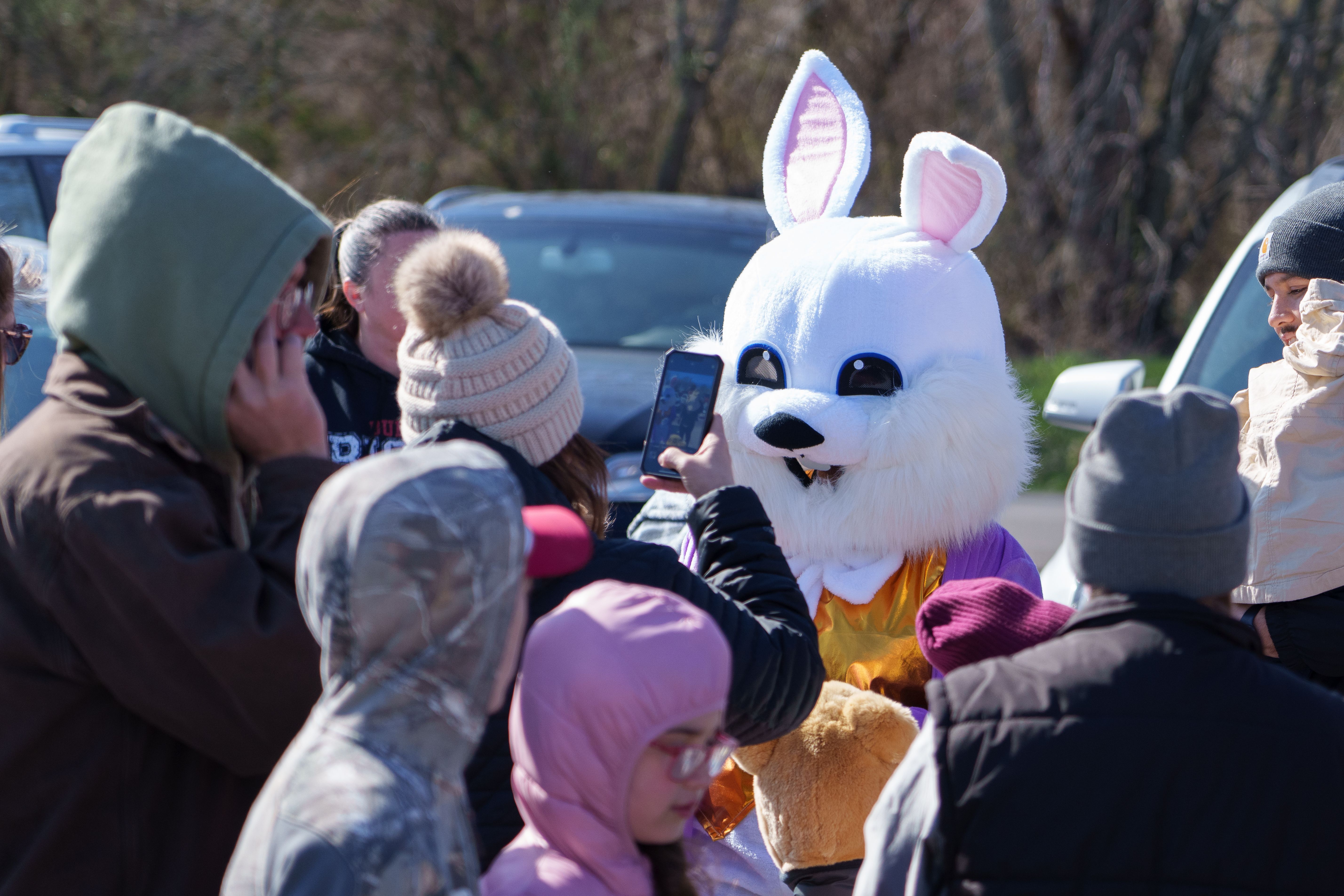 Photo of a crowd surrounding an Easter Bunnny mascot, with the person closest taking a photo