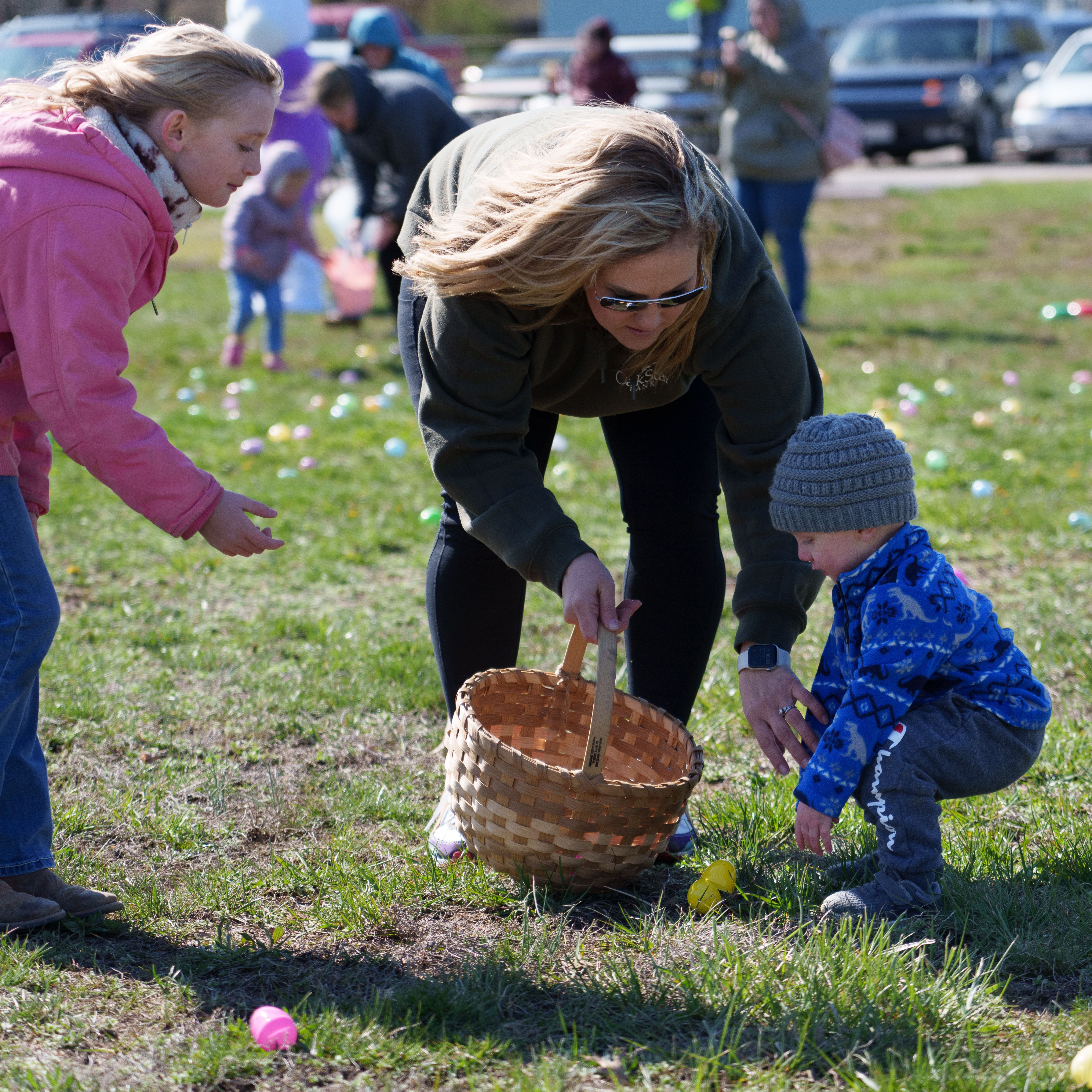 Photo of an older child and an adult helping a small boy collect eggs